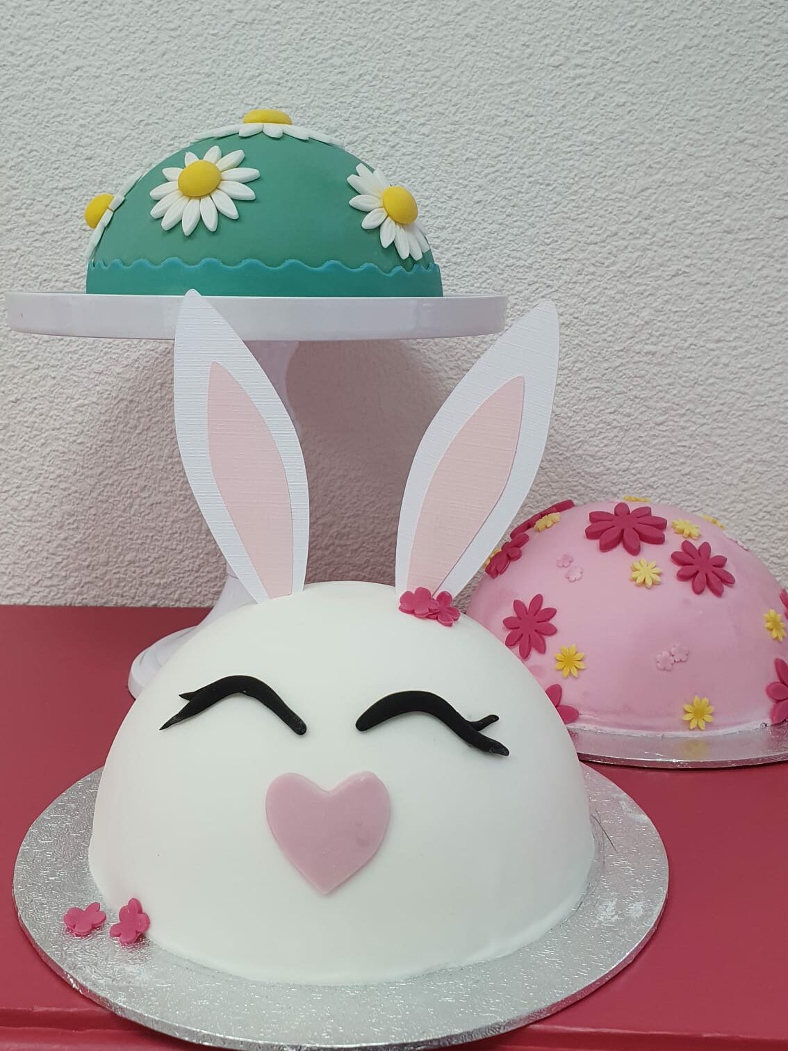 Voorjaars boltaartjes, een groene met madeliefjes, een lichtroze met donkerroze en gele bloemetjes en een wit boltaartje dat gedecoreerd is als een konijntje, met twee oren van papier. Workshop voorjaarstaartje in Kampen op 20 maart 2024